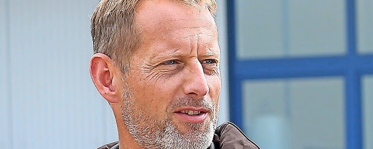 Otmar Birkner AutoGyro A middle-aged man with short, light brown hair and a beard looks to the side. He is outdoors, wearing a brown jacket, with a blurred background showing part of a building and a blue window frame.